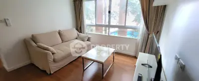 Cozy living room with beige sofa, wooden floor, and large window with curtains.