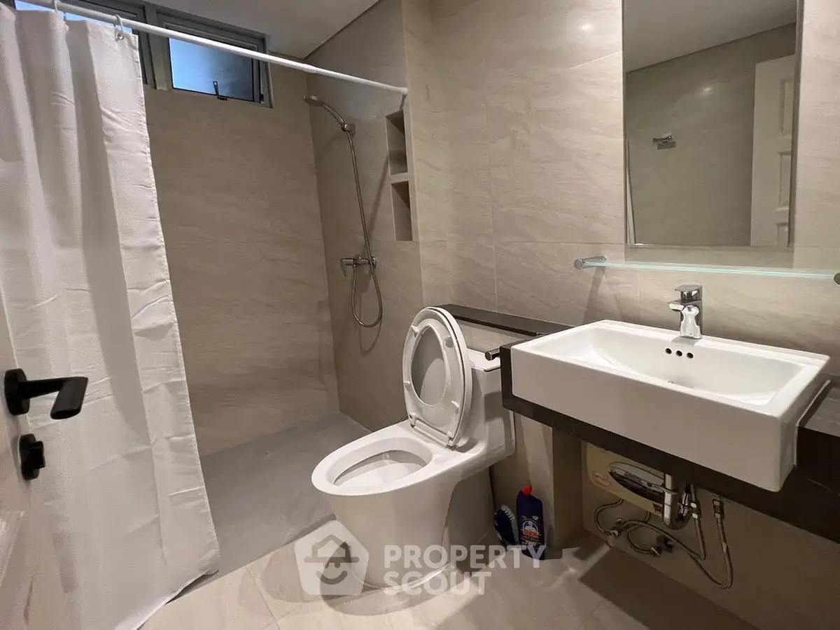 Modern bathroom with sleek fixtures and neutral tones, featuring a shower and a contemporary sink.