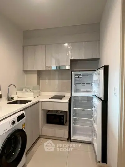 Modern kitchen with open fridge and washing machine, sleek cabinetry and appliances.