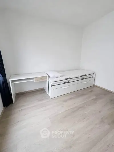 Minimalist bedroom with single bed and desk, featuring light wood flooring and white walls.