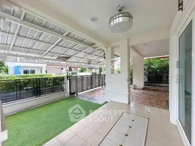 Spacious covered patio with artificial grass and modern ceiling fan, perfect for outdoor relaxation.