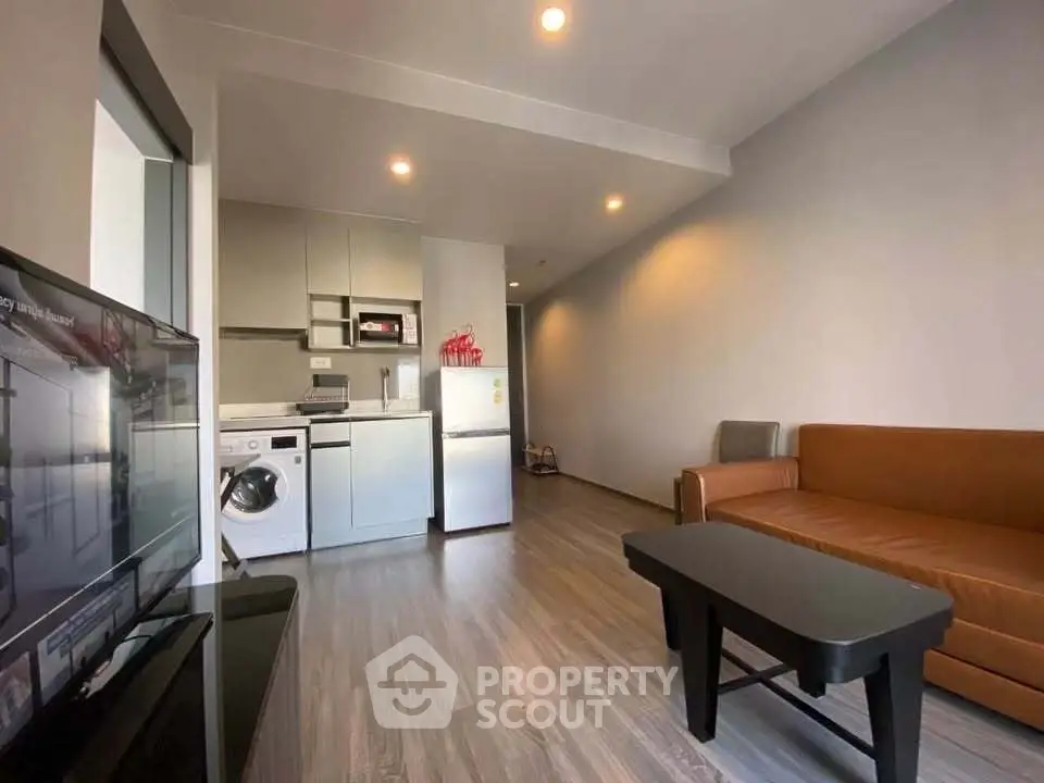 Modern living room with sleek kitchen, washing machine, and cozy seating area in open layout apartment.