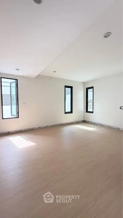 Spacious empty room with large windows and wooden flooring, perfect for customization.