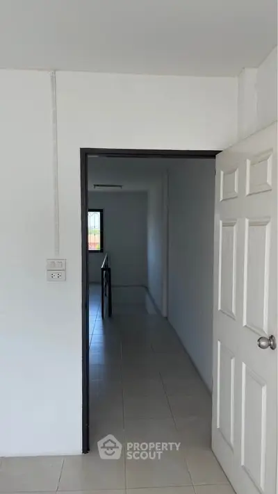 Minimalist interior hallway with white walls and tiled flooring, leading to a window with natural light.