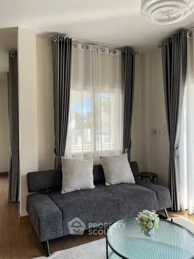 Chic living room with modern gray sofa, elegant curtains, and stylish coffee table in a bright, airy space.