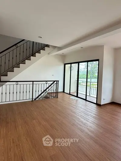 Spacious modern living room with wooden flooring and large windows opening to a balcony.