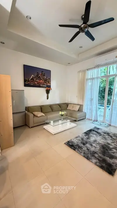 Spacious living room with modern decor and garden view, featuring a cozy sofa and elegant ceiling fan.