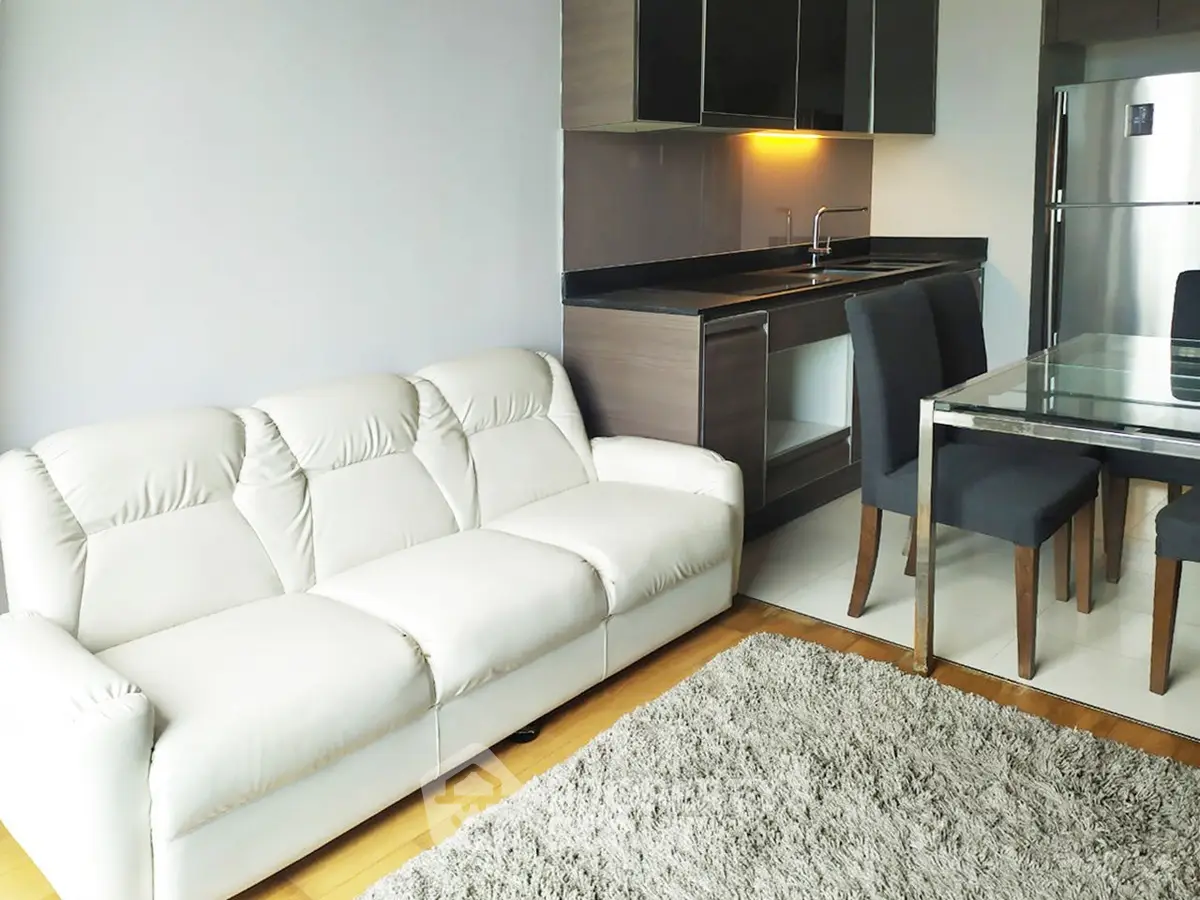 Modern living room with sleek kitchen, featuring a white sofa and dining area with stainless steel appliances.