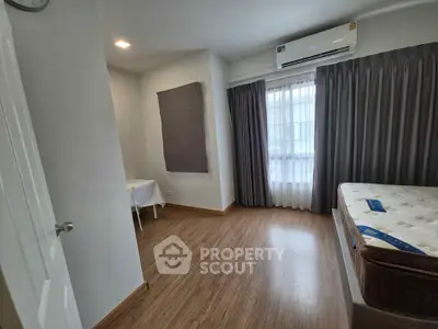Spacious bedroom with wooden flooring and natural light, featuring a comfortable mattress and air conditioning.