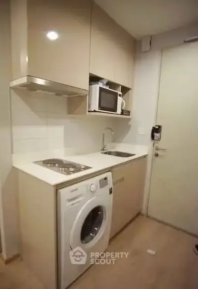 Compact kitchen with integrated washing machine and microwave in modern apartment.