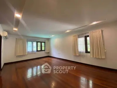 Spacious empty room with wooden floors and large windows, ideal for customization.