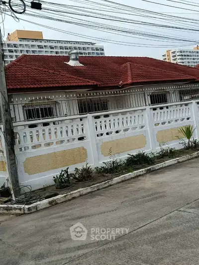 Charming single-story house with red roof and white fence in urban setting.