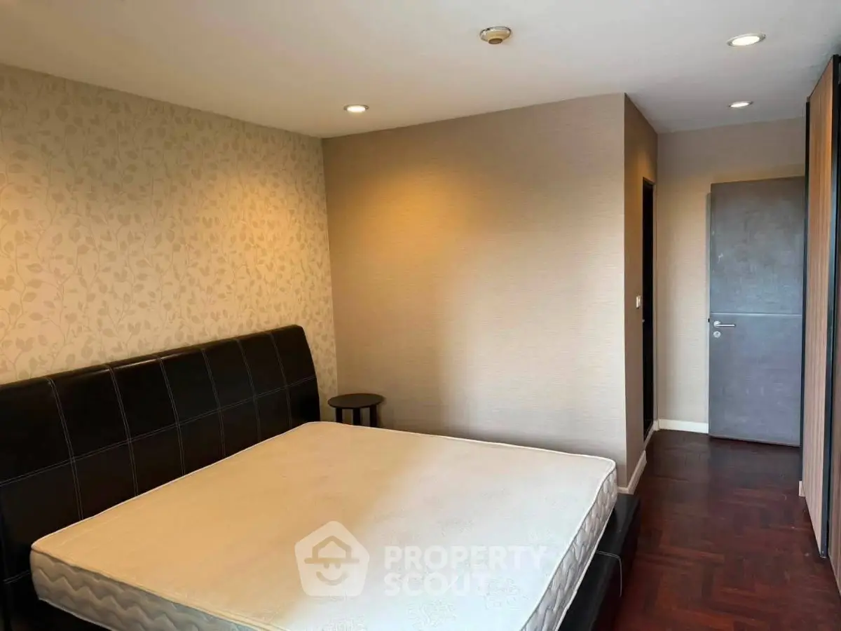 Spacious bedroom with elegant wallpaper and hardwood flooring in modern apartment.