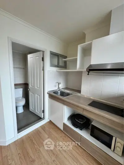 Modern kitchen with wooden flooring and adjacent bathroom, featuring sleek cabinetry and appliances.