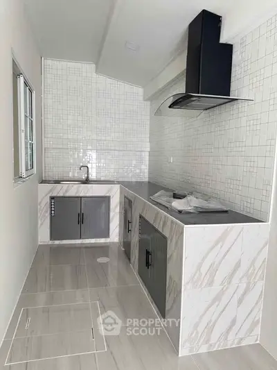 Modern kitchen with sleek cabinetry and tiled backsplash, featuring a built-in range hood and ample counter space.