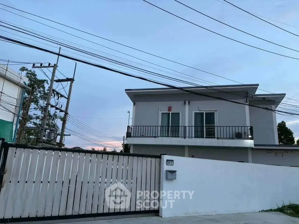 Modern two-story house with balcony and gated entrance at dusk.