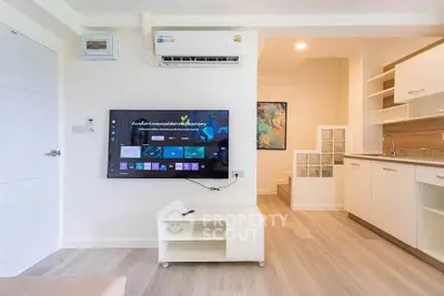 Modern living room with wall-mounted TV and sleek kitchen in open layout apartment.