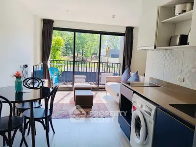 Modern open-plan living room with kitchen, featuring large windows and a washing machine, offering a bright and airy space.