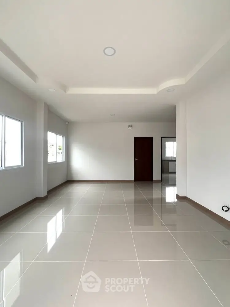 Spacious empty living room with glossy tiled floors and large windows for natural light.