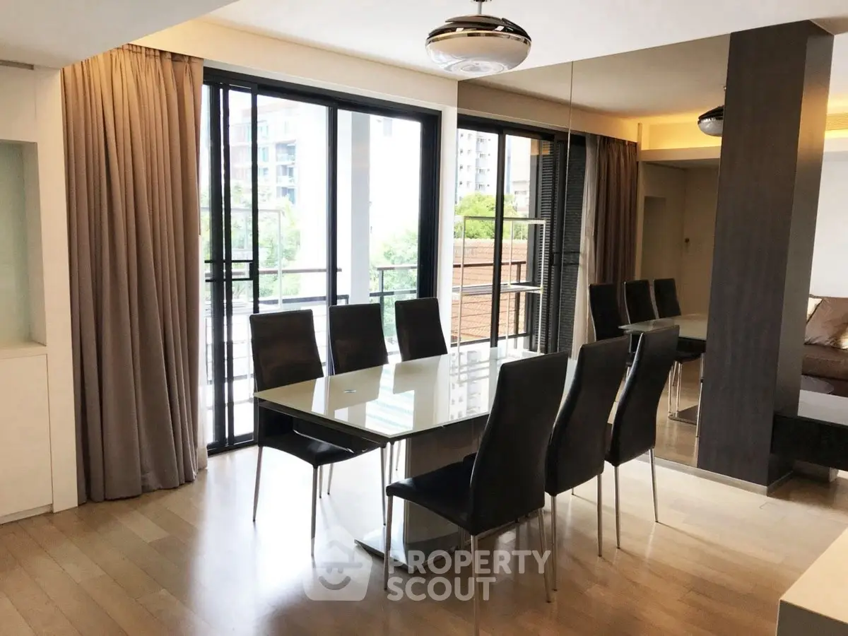 Elegant dining area with modern glass table and sleek chairs, featuring floor-to-ceiling windows and balcony view.