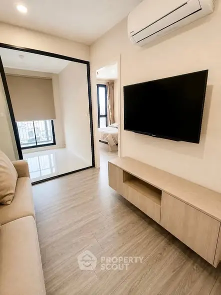 Modern living room with sleek TV setup and air conditioning, leading to a cozy bedroom with natural light.