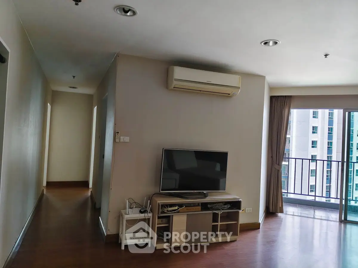 Spacious living room with modern TV setup and balcony view in urban apartment.
