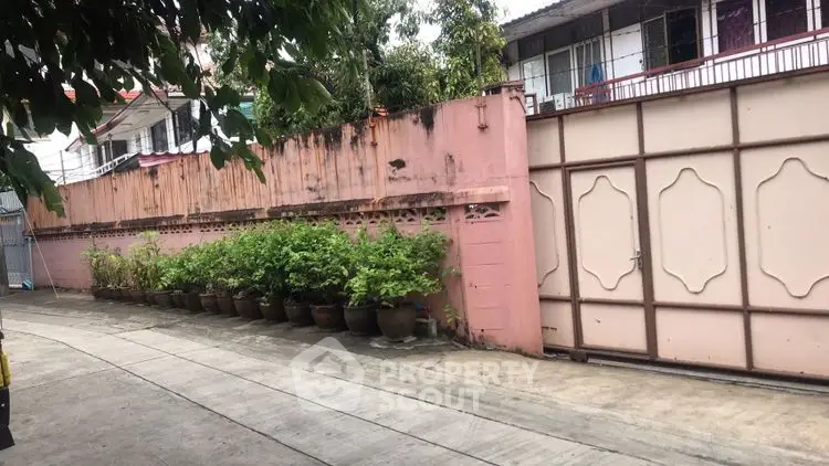 Charming residential exterior with pink wall and potted plants lining the driveway.