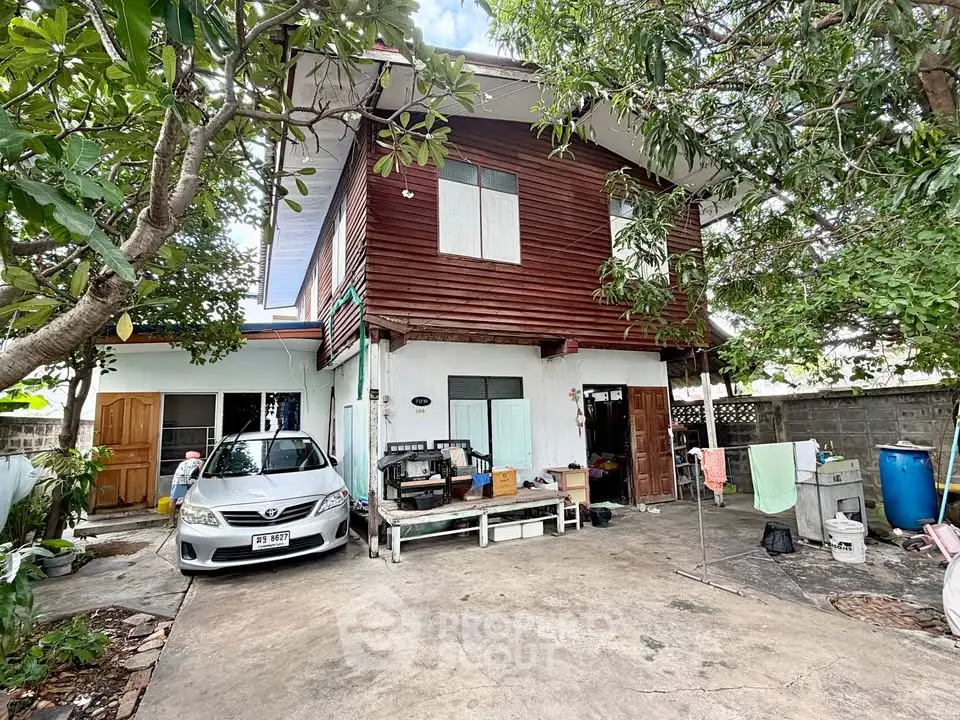 Charming two-story house with wooden facade and spacious driveway, surrounded by lush greenery.
