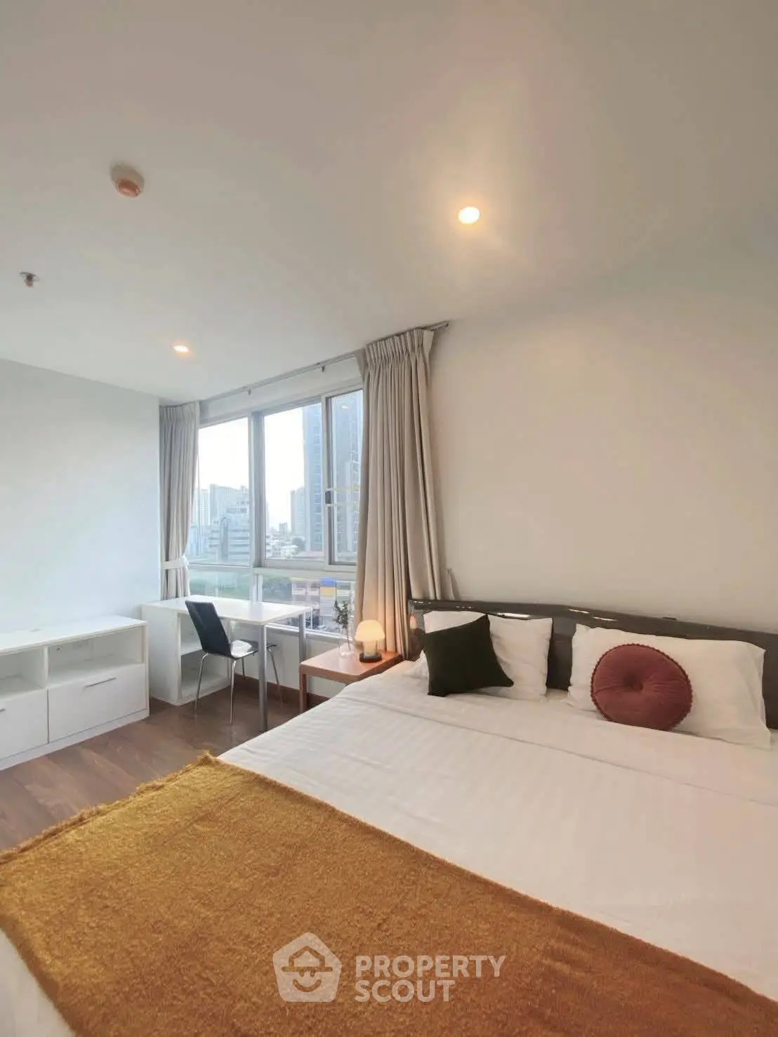 Modern bedroom with city view, featuring a cozy bed, study desk, and large windows for natural light.