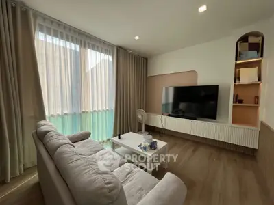 Modern living room with cozy sofa and large TV, featuring elegant curtains and wooden flooring.