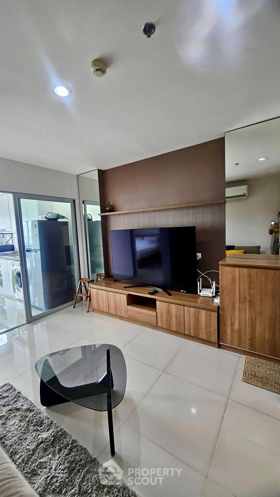 Modern living room with sleek furniture and large TV, featuring glass doors leading to a bright balcony.