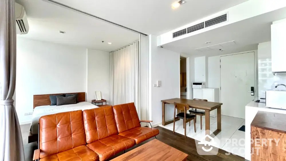 Modern open-plan studio apartment with stylish leather sofa and cozy dining area.