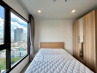 Modern bedroom with large window offering stunning city view, featuring a comfortable bed and sleek wardrobe.