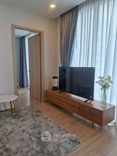 Modern living room with stylish decor and large TV, featuring cozy rug and elegant curtains.