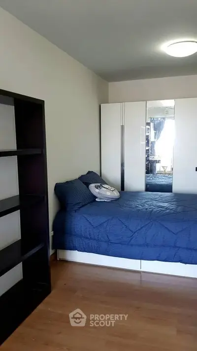 Cozy bedroom with blue bedding, mirrored wardrobe, and wooden flooring.