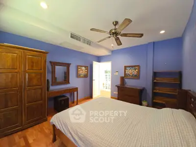 Spacious bedroom with wooden furniture and blue walls, featuring a ceiling fan and ample natural light.