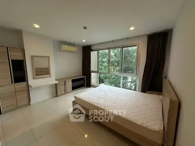 Spacious bedroom with large window and modern furnishings in serene setting.