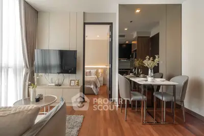 Modern open-plan living room with dining area and bedroom view, featuring sleek furniture and warm wooden flooring.