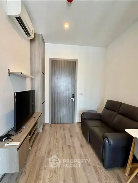 Modern living room with sleek furniture and wooden flooring, featuring a TV and air conditioning.