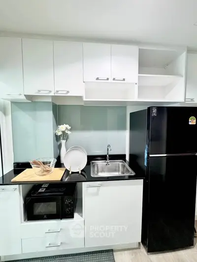 Modern kitchen with sleek black fridge and microwave, featuring white cabinetry and a stylish sink area.