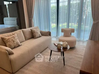 Elegant living room with cozy sofa, stylish armchair, and garden view through large windows.