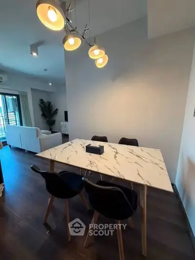 Modern dining area with marble table and stylish lighting in open-plan living space.