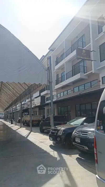 Modern multi-story building with parking area and covered walkway in sunny setting.