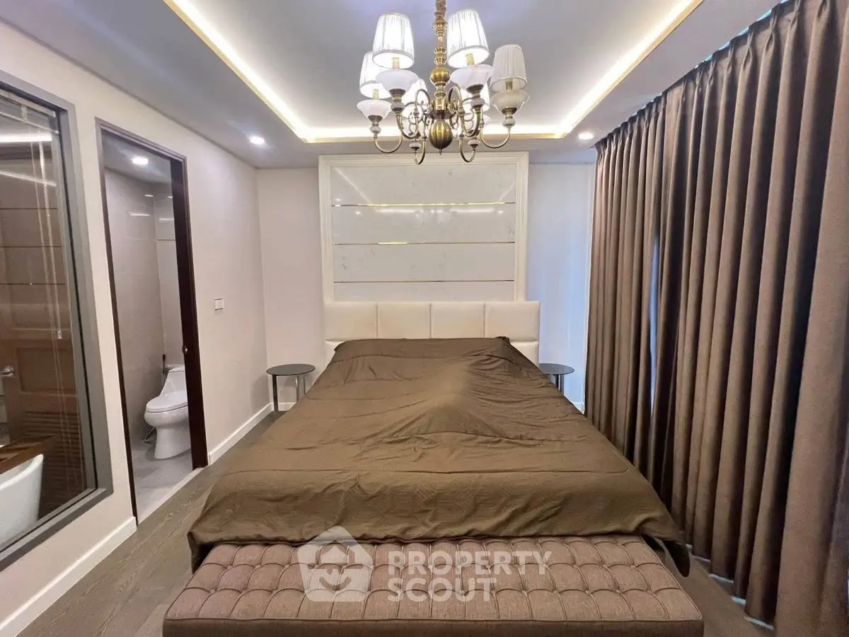Luxurious bedroom with elegant chandelier and en-suite bathroom, featuring modern design and cozy ambiance.