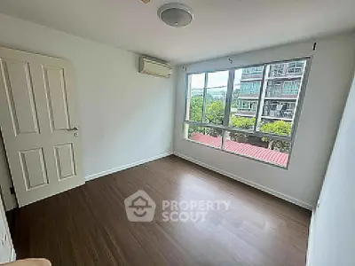 Spacious empty bedroom with large window and wooden flooring, offering a bright and airy atmosphere.