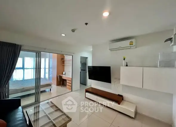 Modern living room with sleek furniture and open layout leading to a cozy bedroom.