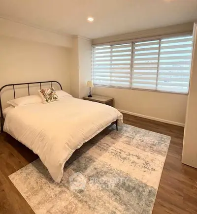 Spacious bedroom with large window and cozy decor in modern apartment.