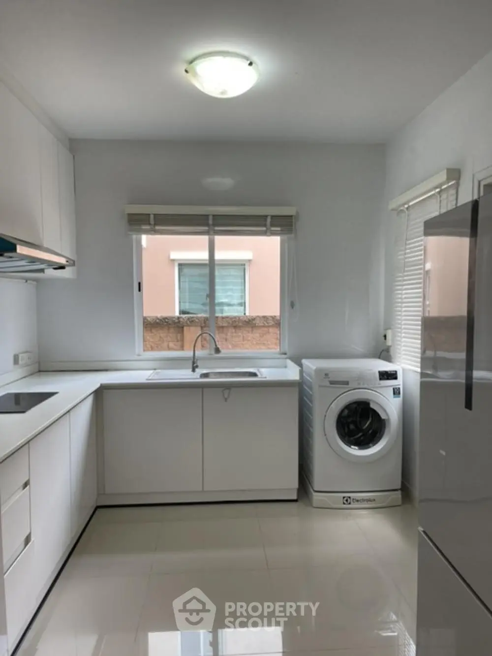 Bright and modern kitchen with sleek white cabinetry and appliances, featuring a convenient washing machine and ample natural light.