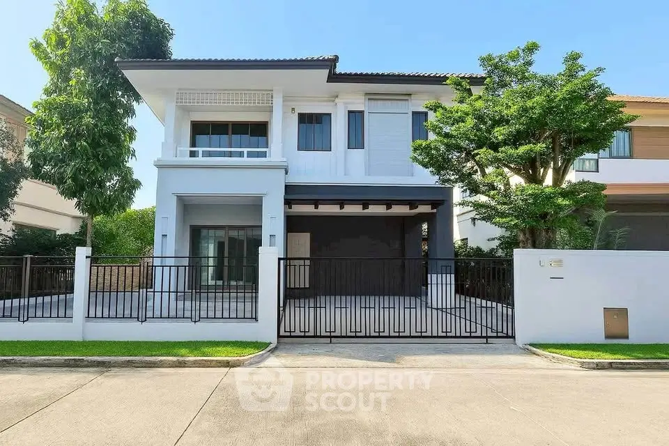 Modern two-story house with gated entrance and lush greenery