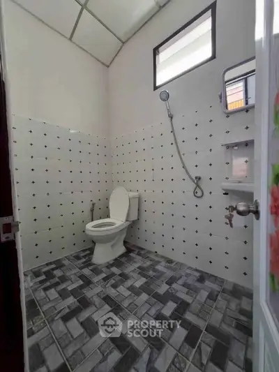 Modern bathroom with tiled walls and floor, featuring a toilet and shower area.